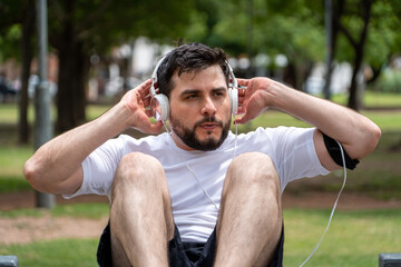 Hombre entrenando concentrado en el parque, haciendo abdominales mientras escucha música durante...