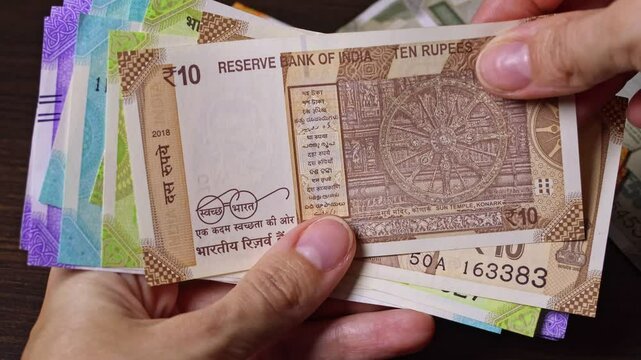 Female hands hold Indian national currency banknotes. Close-up top view of Indian paper notes of 10 rupees (INR) from both sides. Real time motion video.