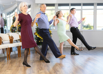 Naklejka premium Happy adult people dancing Irish folk dance in row at modern ballroom on Christmas