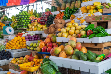 Vibrant fruit and vegetable stand at a traditional market. Fresh mangoes, avocados, peppers, pineapples, and citrus fruits arranged in wooden crates.