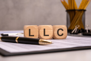 wooden blocks spelling "LLC" on a desk with office documents, a pen, and stationery items