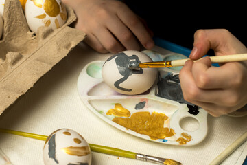 Hands meticulously paint an Easter egg with a brush, surrounded by colorful eggs and art supplies. Perfect for Easter crafts, artistic expression, or holiday traditions.