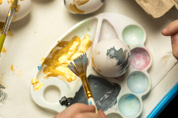 A close-up of hands painting an Easter egg with vibrant hues, with decorated eggs in the background. Ideal for festive creativity, spring art, or family crafting moments.
