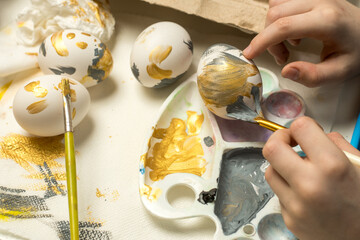 Hands carefully paint an Easter egg with a brush, surrounded by painted eggs and art supplies. Suitable for holiday creativity, Easter decor, or artistic expression.