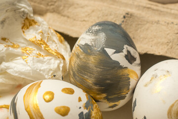 Close-up of beautifully decorated Easter eggs with golden and black paint splashes, surrounded by crumpled paper and an egg carton, perfect for holiday celebrations.