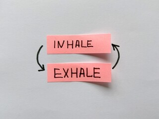 Two pink sticky notes with handwritten words “inhale” and “exhale,” connected by curved...
