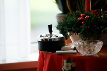 Elegant holiday gathering decor with an ashtray and festive greenery on a red tablecloth near a bright window