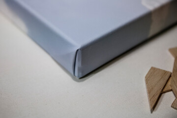 Curved edge of a wrapped canvas on a neutral surface with wooden pieces scattered nearby in a creative workspace