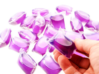 Liquid detergent in hand over a purple color washing pods on white background. Hygiene product for...