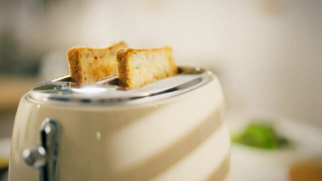 Two slices of bread are toasting in a sleek toaster placed on a kitchen counter. The bright and inviting atmosphere suggests morning activity and meal preparation