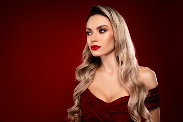 Fototapeta premium Glamorous blond woman in elegant burgundy evening dress against a deep red background