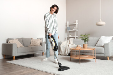 Happy young woman cleaning carpet with handheld vacuum cleaner in living room