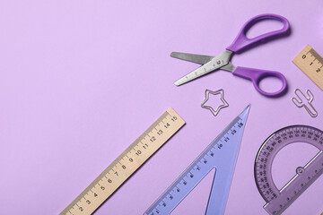 Different rulers with scissors and paper clips on purple background