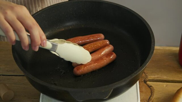 Chef ensures that sausages made from meat do not burn by turning them over during frying process in a frying pan, using tongs.