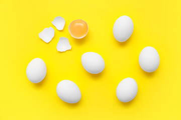 Whole and cracked chicken eggs on yellow background