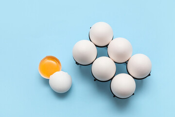 Holder with whole and cracked chicken eggs on blue background