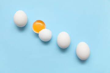 Whole and cracked chicken eggs on blue background