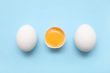 Whole and cracked chicken eggs on blue background