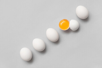 Whole and cracked chicken eggs on grey background