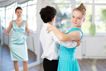 Girl and a boy in festive clothes learn to dance tango under guidance of a teacher