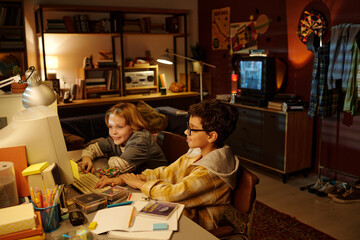 Two children sitting at a desk enjoying video games on old computer in a cozy, well-furnished room...