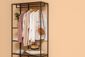Rack with clothes and shoes near beige wall