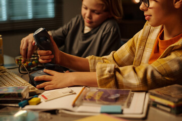 Children engaging in immersive gaming session, holding joystick which is plugged into computer setups, surrounded by various gadgets, books, and other study materials
