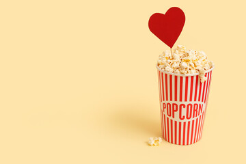 Bucket of popcorn and paper heart on yellow background. Valentine's Day celebration