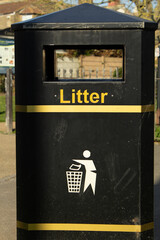 A black trash bin with yellow stripes in the park.