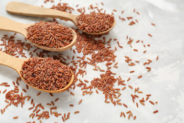 Wooden spoons with raw brown rice on white grunge background