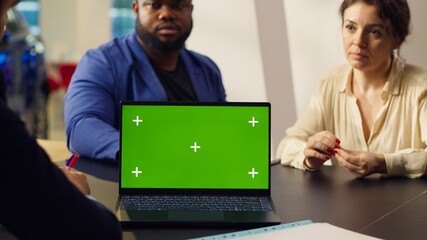 Customers in showroom looking for new vehicle to purchase, being shown options by salesman on mockup laptop. Agent using green screen notebook to help clients evaluate cars, camera A