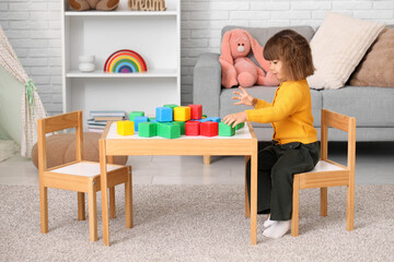 Cute little girl with plastic cubes at table in living room