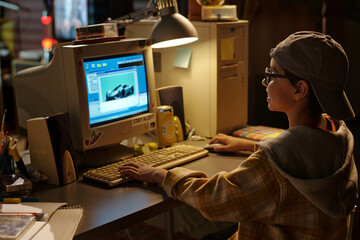 Young person sitting at desk using vintage computer in bedroom. Retro-style gaming scene with...