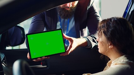 Showroom salesman showing car brochure and price list on green screen tablet to clients after they finished test drive. Dealership agent showing vehicle catalog to customers on mockup device, camera A