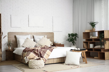 Interior of light bedroom with bedside table, houseplants, shelving unit and bed