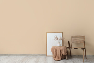 Comfortable wooden chair with frame, blanket and vase near beige wall