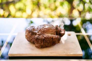 Juicy roast beef lies on a wooden cutting board on a table on the balcony