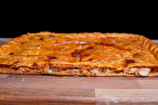 Delicious empanada gallega resting on wooden cutting board, displaying its filling