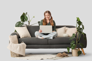 Young woman with laptop sitting on black sofa against white background