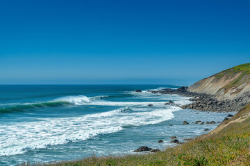 A stunning ocean wave crashing under a clear blue sky, capturing the beauty and power of nature in vibrant colors. A powerful wave breaks in the vast ocean under a clear blue sky, creating a stunning