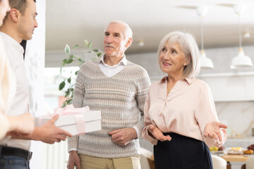 Obraz premium Happy senior man and woman welcoming young couple during small gathering with family members at home