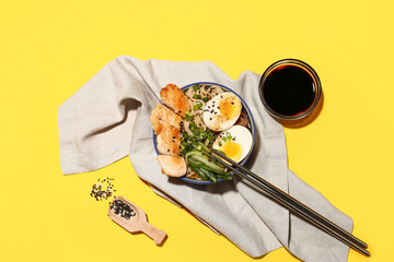 Bowl of ramen noodle soup with chicken and cucumber slices on yellow background