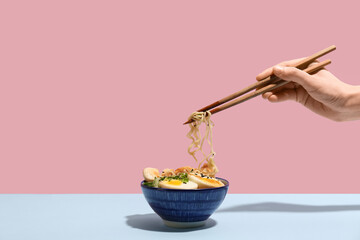 Female hand with chopsticks and bowl of ramen noodle soup on colorful background