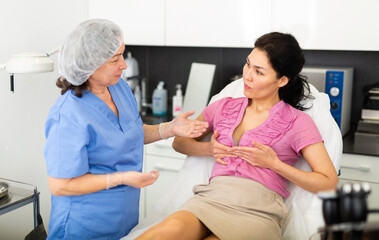 Fototapeta premium Experienced cosmetology doctor tells a young female patient about the health of the female breast, explaining how to ..properly care for it to maintain a beautiful shape