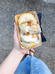 Top view of woman's hand holding a disposable plate with dumplings with sour cream and dried onion. Traditional Ukrainian Food. Street Food.