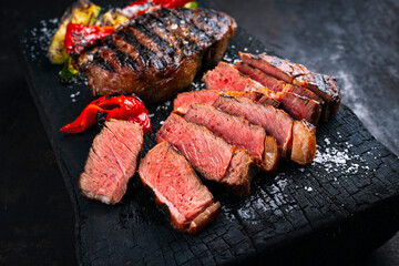 Traditional barbecue dry aged Wagyu rib eye beef steak with grilled paprika and zucchini served as close-up on a charred wooden board