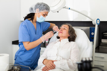 Obraz premium Qualified focused cosmetologist giving beauty injections for face skin rejuvenating and tightening for elderly female client in aesthetic medicine office