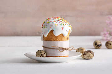 Plate with sweet Easter cake and quail eggs on white wooden background