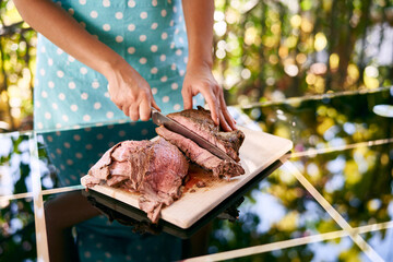 Woman in an apron cuts thin slices of roast beef on a cutting board with a large knife