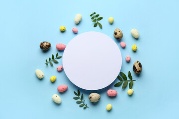 Frame made of green leaves, Easter eggs and blank card on turquoise background